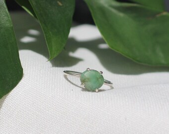 May include: A silver ring with a green gemstone set in a prong setting.
