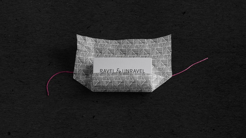 May include: A white paper package with a geometric pattern and a label that reads "RAVEL & UNRAVEL". The package is tied with a pink string.