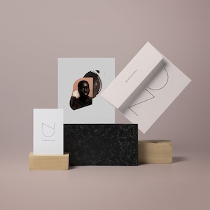 May include: A black and white illustration of a stylized face with a circle and a triangle. The illustration is on a white card with the text "And breathe." The card is on top of a black and white textured surface. A white card with the text "CZ urban spa" is on a wooden surface.
