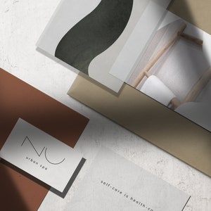 May include: A flat lay of branding materials for a spa. The image features a brown card with the text "NU urban spa" in black lettering, a white card with the text "self-care is health-co" in black lettering, a white card with a black abstract design, and a white card with a photo of a wooden chair with a white towel on it and the letter "Z" in black lettering.