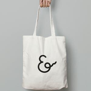 May include: A white canvas tote bag with black handles and a black ampersand logo.