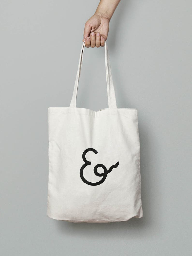 May include: A white canvas tote bag with black handles and a black ampersand logo.