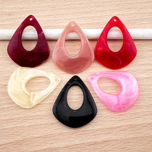 Könnte beinhalten: Sechs tropfenförmige Harz-Anhänger mit einem Loch oben. Die Anhänger sind in verschiedenen Farben, darunter Rot, Pink, Schwarz und Weiß.