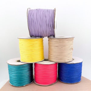 Pode incluir: Seis rolos de corda colorida enrolados em torno de rolos de cartão. As cores são lavanda, amarelo, beige, azul-petróleo, rosa e azul.