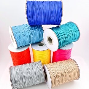Op de afbeelding: Acht spoelen met gekleurde elastische koord, gerangschikt in een piramidevorm. De kleuren zijn blauw, lichtblauw, teal, geel, roze, rood, grijs en beige.