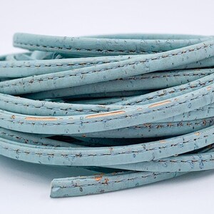 May include: A roll of light blue cork cord with a stitched edge. The cord is made from natural cork and has a subtle texture.