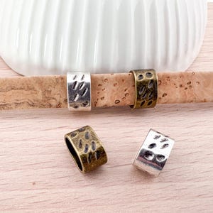 Könnte beinhalten: Vier silberne und bronzene Metallringe mit einem strukturierten Design. Die Ringe liegen auf einer Korkoberfläche.
