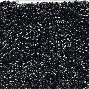 May include: A close-up of a pile of small, black, cylindrical beads. The beads are densely packed together, filling the frame. Each bead has a small hole running through its centre, and they have a glossy finish.