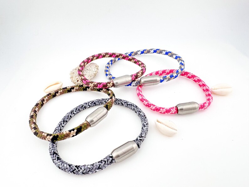 Puede incluir: Cinco pulseras trenzadas de colores con cierres magn&eacute;ticos. Las pulseras est&aacute;n hechas de cordones de diferentes colores y tienen un cierre magn&eacute;tico plateado.