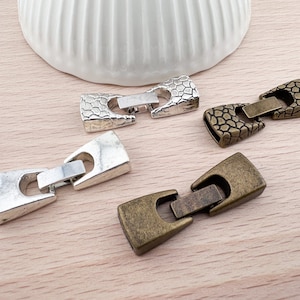 Op de afbeelding: Drie metalen sluitingen voor het maken van sieraden. De sluitingen zijn zilver, antiek zilver en antiek messing. Elke sluiting heeft een getextureerd oppervlak en een rechthoekige vorm.