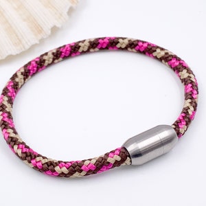 Puede incluir: Un brazalete de cuerda trenzada rosa, marr&oacute;n y beige con un cierre magn&eacute;tico plateado.