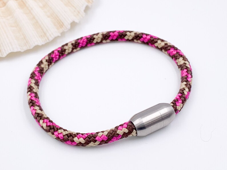 Puede incluir: Un brazalete de cuerda trenzada rosa, marr&oacute;n y beige con un cierre magn&eacute;tico plateado.