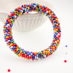 Könnte beinhalten: Ein farbenfrohes Perlenarmband mit Spiralmuster. Das Armband besteht aus kleinen, runden Perlen in verschiedenen Farben, darunter Rot, Blau, Gelb und Grün. Das Armband hat einen Umfang von etwa 18 cm.