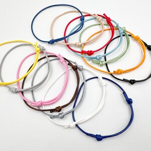 May include: A collection of colorful, adjustable string bracelets. The bracelets are in various colors, including blue, red, yellow, and pink. Each bracelet features a simple knot closure. These bracelets are a simple and versatile accessory.