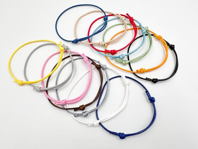 May include: A collection of colorful, adjustable string bracelets. The bracelets are in various colors, including blue, red, yellow, and pink. Each bracelet features a simple knot closure. These bracelets are a simple and versatile accessory.