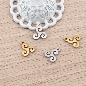 Op de afbeelding: Vier metalen bedels in de vorm van een drievoudige spiraal, twee goud en twee zilver. De bedels liggen op een houten oppervlak.