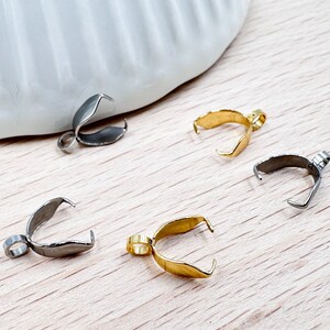 Peut inclure: Quatre fermoirs en métal argenté et doré pour la fabrication de bijoux. Les fermoirs ont la forme d'une larme et sont dotés d'une petite boucle en haut.