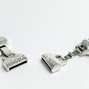 May include: Two silver-toned metal clasps with a textured surface. The clasps are designed to be used for jewellery making or other craft projects.