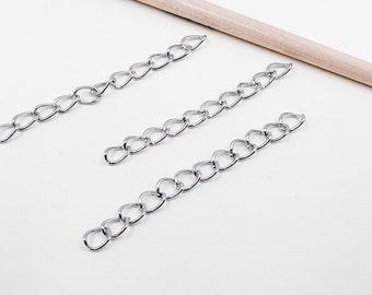 Peut inclure: Trois chaînes argentées avec des maillons en forme de cœur. Les chaînes sont disposées sur une surface blanche.
