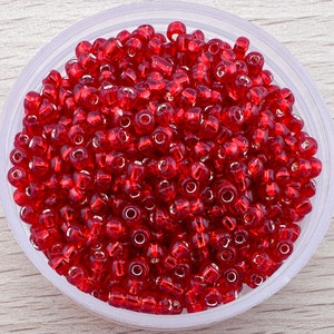 Könnte beinhalten: Eine Schale gefüllt mit roten Glasperlen. Die Perlen sind klein und rund, mit einem glänzenden Finish.