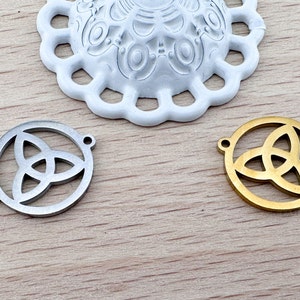 Op de afbeelding: Twee metalen bedels met een Keltisch knoopontwerp. Een bedel is zilver en de andere is goud.