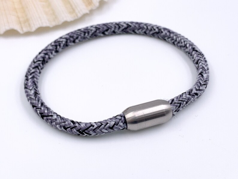 Puede incluir: Un brazalete trenzado gris con un cierre magn&eacute;tico plateado.