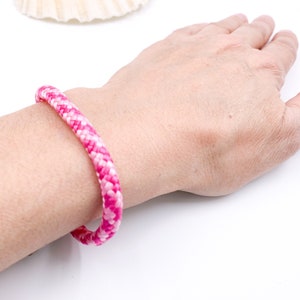 Puede incluir: Un brazalete de cuerda trenzada rosa y blanco en la mu&ntilde;eca de una persona.