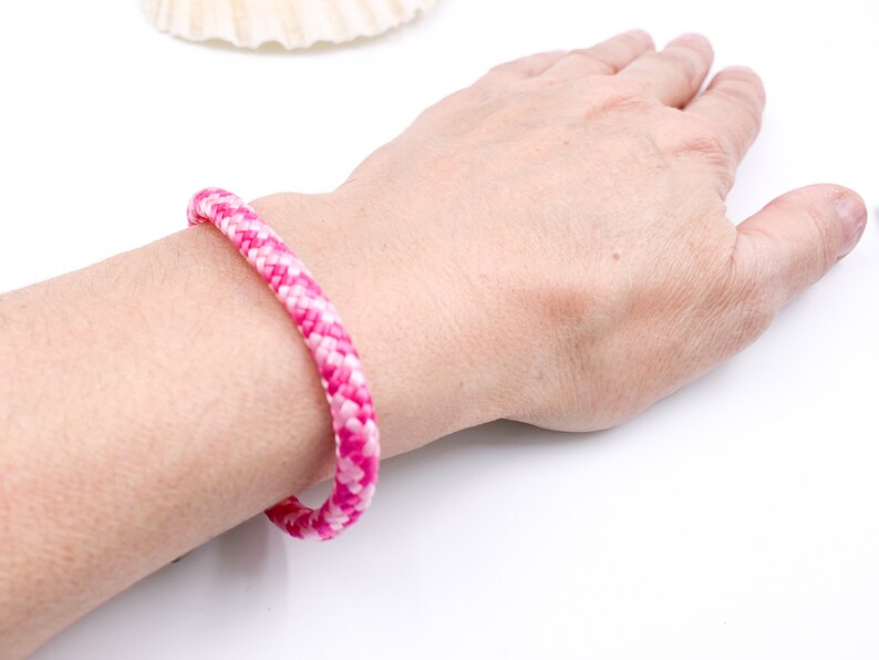 Puede incluir: Un brazalete de cuerda trenzada rosa y blanco en la mu&ntilde;eca de una persona.