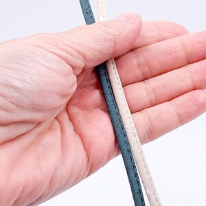 May include: Two cords of cork fabric, one is teal blue and the other is a light beige colour.