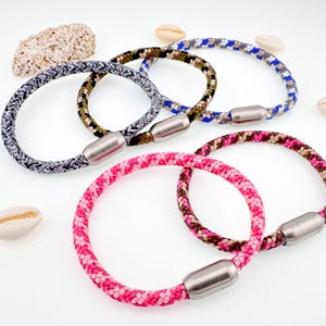 Puede incluir: Cuatro pulseras de cuerda de colores con cierres magn&eacute;ticos. Las pulseras son grises, azules, verdes y rosas.