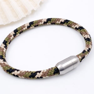 Puede incluir: Un brazalete de paracord con estampado de camuflaje y cierre magn&eacute;tico de acero inoxidable.