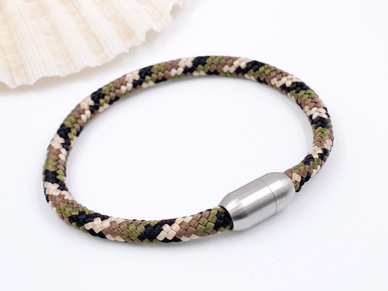Puede incluir: Un brazalete de paracord con estampado de camuflaje y cierre magn&eacute;tico de acero inoxidable.