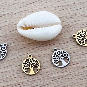 Pode incluir: Quatro pingentes de prata e ouro em forma de árvore da vida sobre uma superfície de madeira. Os pingentes são redondos e apresentam um design de árvore detalhado.
