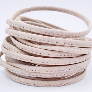 May include: A close-up of a roll of off-white cork cord with a stitched seam. The cord is rolled into a circle and is about 1.2 cm wide.
