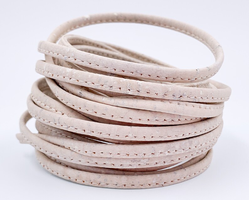 May include: A close-up of a roll of off-white cork cord with a stitched seam. The cord is rolled into a circle and is about 1.2 cm wide.