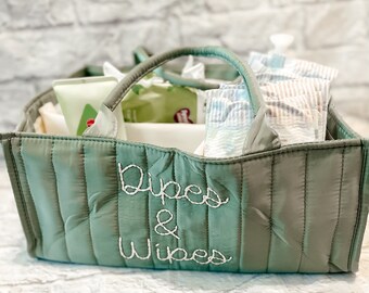 May include: A green quilted diaper bag with the words "Diapers & Wipes" embroidered on the front. The bag is filled with diapers, wipes, and other baby essentials.