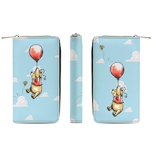 May include: A light blue wallet featuring a cartoon bear holding a red balloon, with bees and clouds on the front and back. The wallet has a zipper closure and a solid light blue spine.