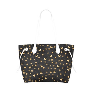 K&ouml;nnte beinhalten: Eine schwarze Tragetasche mit wei&szlig;en Henkeln und einem goldenen Tupfenmuster mit Mickey-Maus-K&ouml;pfen.