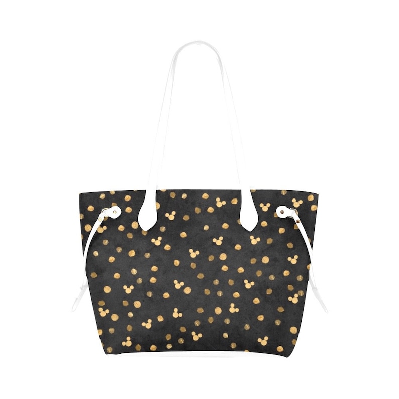 K&ouml;nnte beinhalten: Eine schwarze Tragetasche mit wei&szlig;en Henkeln und einem goldenen Tupfenmuster mit Mickey-Maus-K&ouml;pfen.