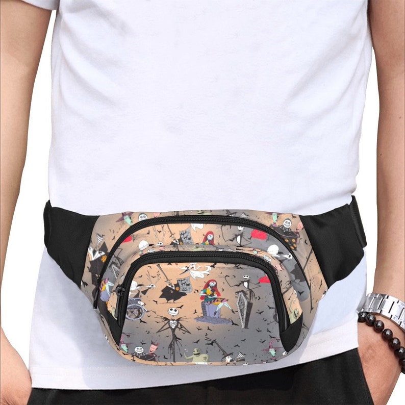 May include: A black fanny pack with a zippered pocket and a colorful print of characters from the Nightmare Before Christmas movie. The print features Jack Skellington, Sally, and other characters from the film.