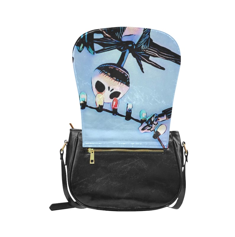 Puede incluir: Bolso de hombro de cuero negro con una solapa que se abre para revelar un forro impreso en azul y blanco con un personaje de dibujos animados colgado de luces navide&ntilde;as.