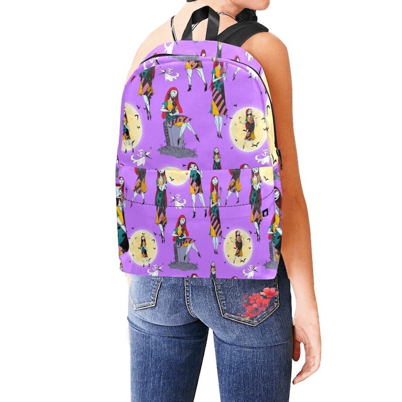 Op de afbeelding: Paarse rugzak met een herhalend patroon van Sally uit The Nightmare Before Christmas. Sally draagt haar patchworkjurk en zit op een grafsteen. De achtergrond is paars met witte vleermuizen en een gele maan.