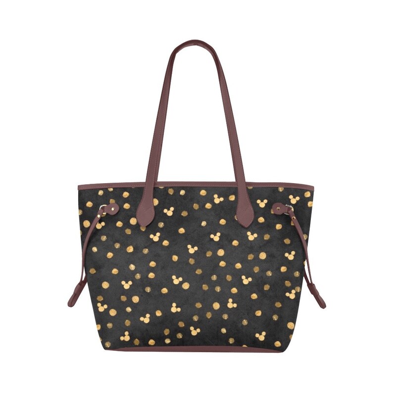 K&ouml;nnte beinhalten: Schwarze Tragetasche mit goldenen Punkten und Mickey-Maus-K&ouml;pfen. Die Tasche hat braune Ledergriffe und einen Kordelverschluss.