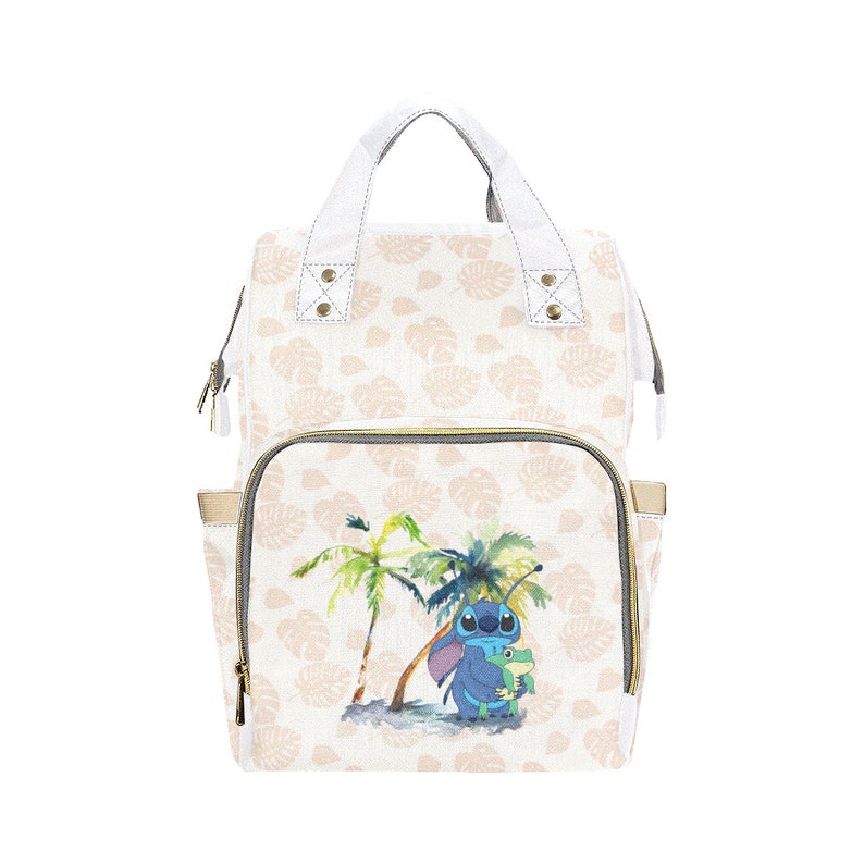 Puede incluir: Una bolsa de pa&ntilde;ales blanca con un estampado de hojas tropicales rosa claro y blanco. La parte delantera de la bolsa presenta un personaje azul Stitch de Lilo & Stitch sosteniendo una rana verde.