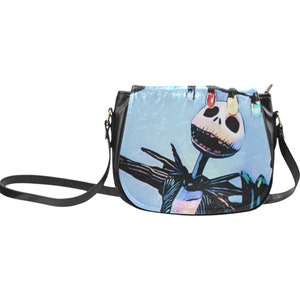 Puede incluir: Un bolso bandolera de imitaci&oacute;n de cuero negro con un estampado azul y blanco de Jack Skellington de Pesadilla Antes de Navidad. El estampado presenta a Jack Skellington con luces de Navidad.