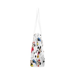Puede incluir: Bolsa de mano blanca con estampado de Mickey Mouse de colores. La bolsa tiene dos asas blancas.