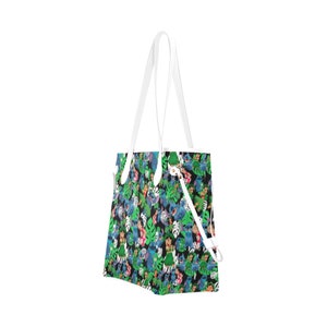 May include: A white tote bag with a colorful print of cartoon characters and tropical leaves. The print features blue, green, pink, and yellow colors.