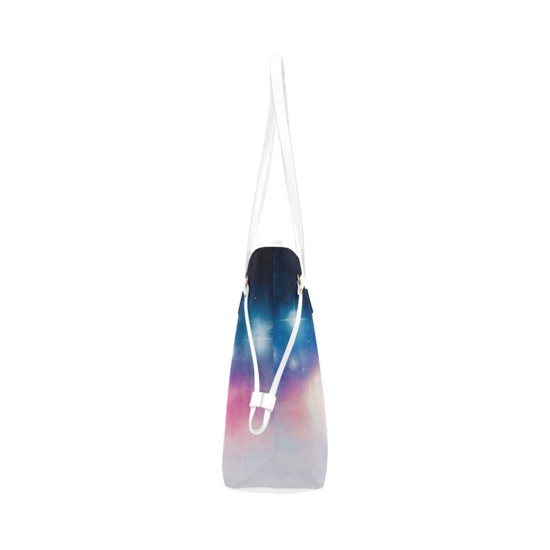 May include: A white tote bag with a galaxy print. The print features a dark blue background with white stars and a pink and purple gradient at the bottom.