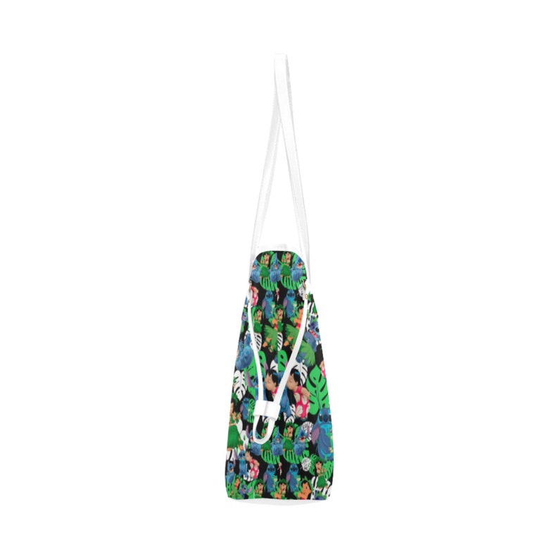 May include: A white tote bag with a black background and a colorful pattern of cartoon characters and tropical leaves. The characters are blue, green, orange, and pink.
