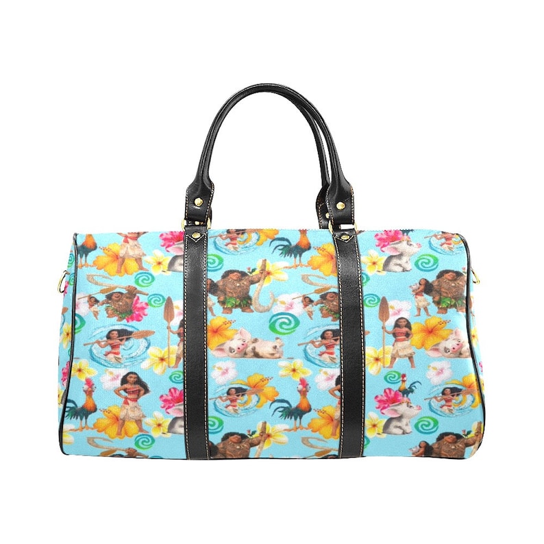 Puede incluir: Una bolsa de viaje azul y blanca con un asa y ribetes de cuero negro. La bolsa presenta un patr&oacute;n repetido de personajes de la pel&iacute;cula animada Moana, incluyendo a Maui, Moana, Pua el cerdo y Hei Hei el gallo.